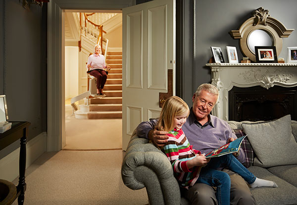 grandpa reading a book to grand daughter while grandma watches on acorn stairlift